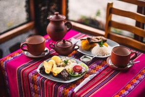 A table set with a meal, including rice, vegetables, and a meat dish, on a colorful tablecloth.