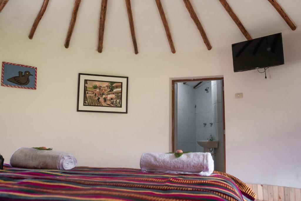 Habitació amb un llit, dues tovalloles, un quadre amb marc, una televisió i una porta.