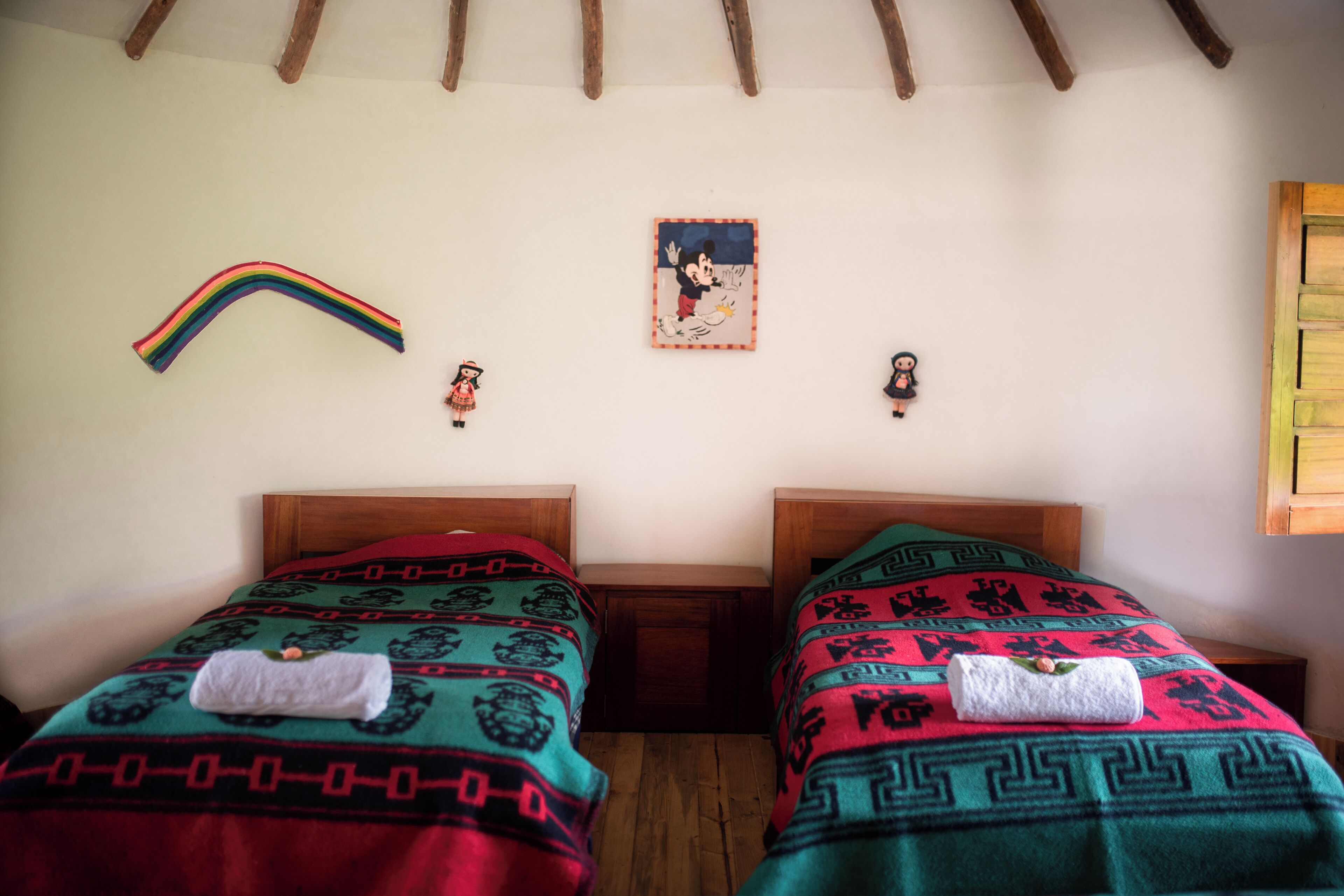 A room with two beds, each with a patterned blanket and a towel. There is a rainbow decoration on the wall and a Mickey Mouse poster.
