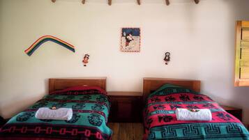 A room with two beds, each with a patterned blanket and a towel. There is a rainbow decoration on the wall and a Mickey Mouse poster.