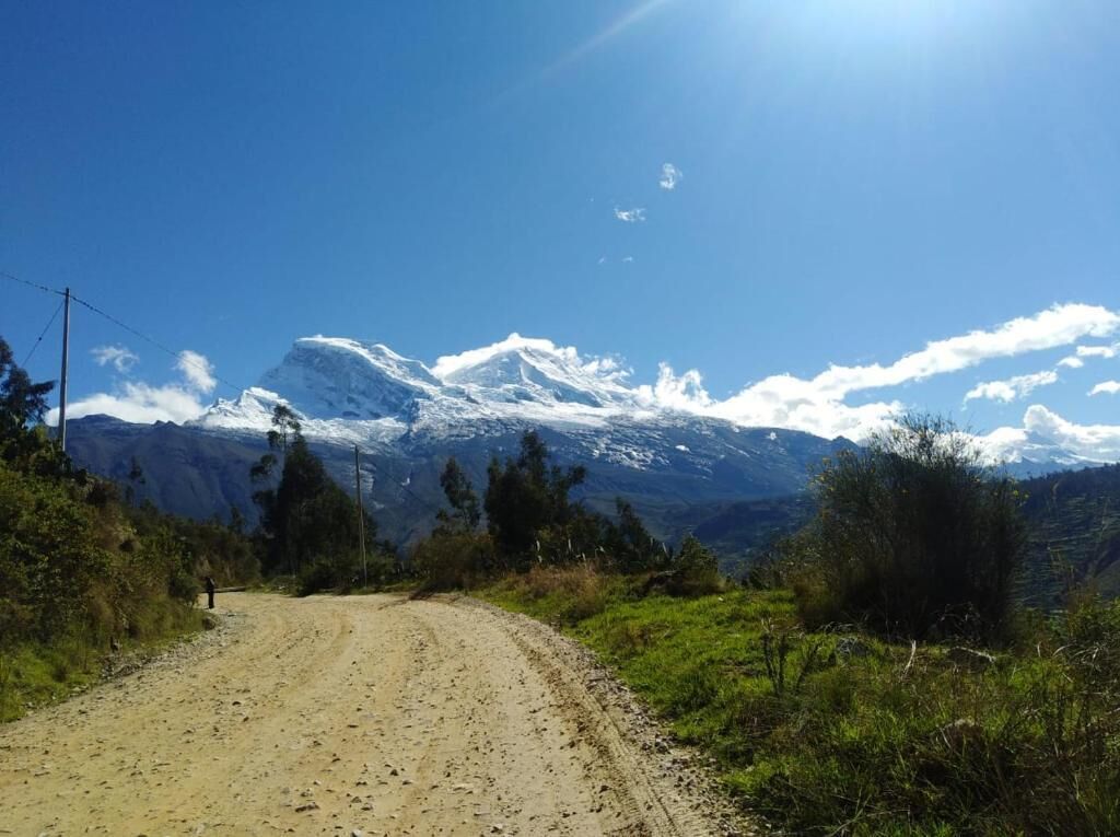 A dirt road leading to a mountain with snow-capped peaks under a clear blue sky.