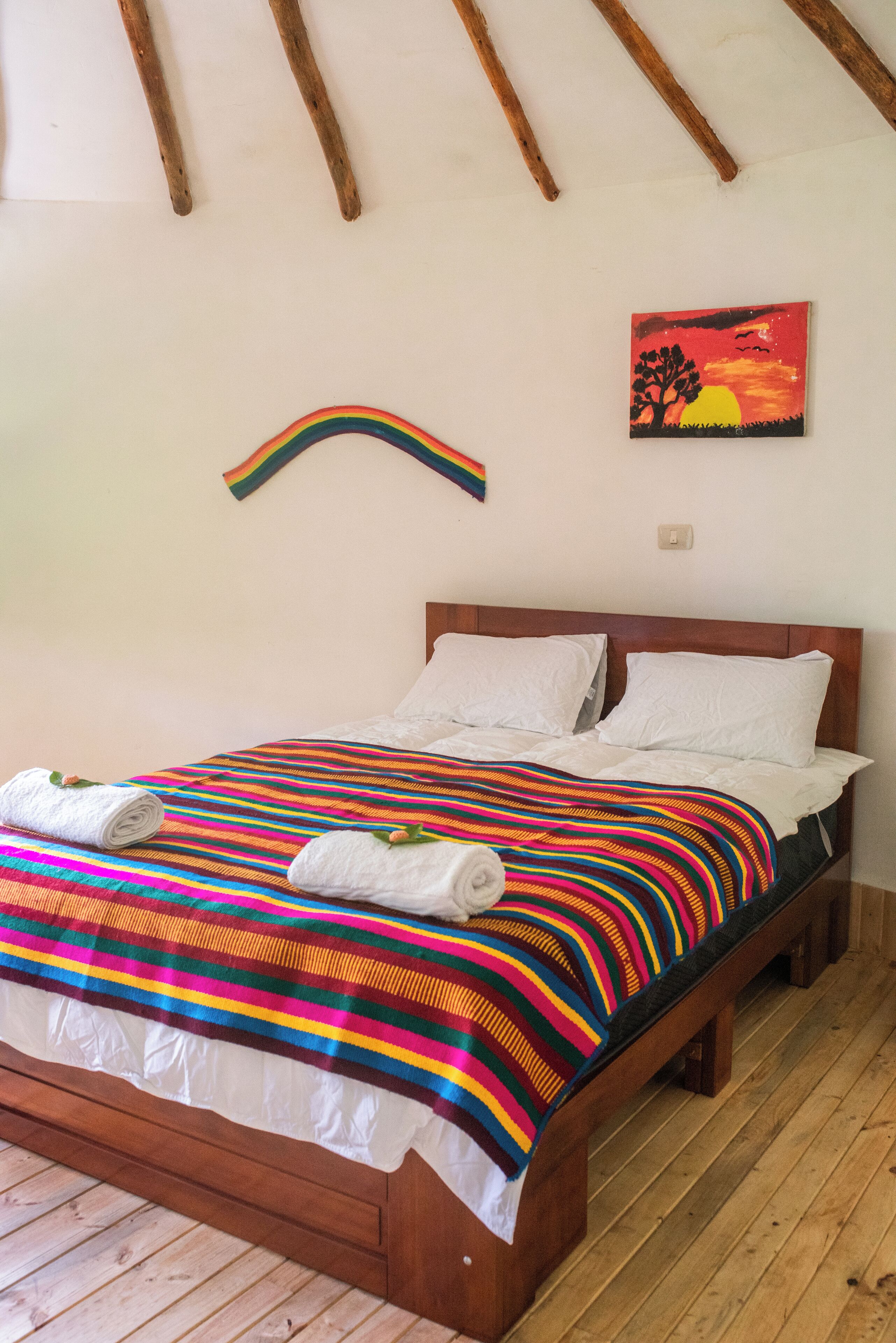 A bed with a colorful striped blanket, white pillows, and rolled towels.