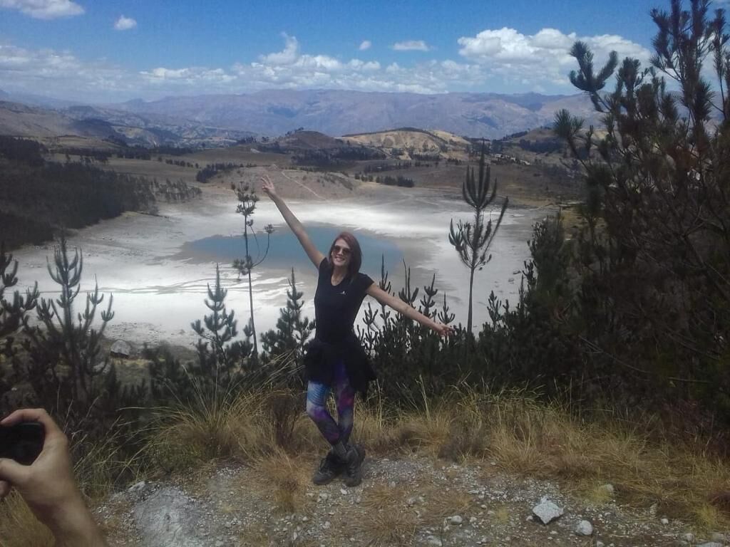 A person standing on a rocky terrain with a view of a lake and mountains in the background.