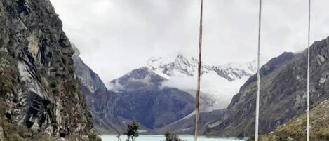 A white SUV parked near a rocky cliff with a lake and mountains in the background.