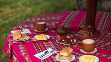Een picknickopstelling met een tafel bedekt met een kleurrijke streepjes tafelkleed, met borden eten, een theepot en kopjes.