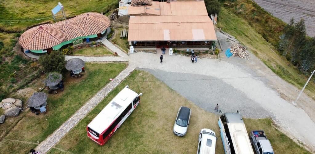 Vue aérienne d’un terrain de camping avec un grand bâtiment, un autobus rouge et plusieurs voitures garées.