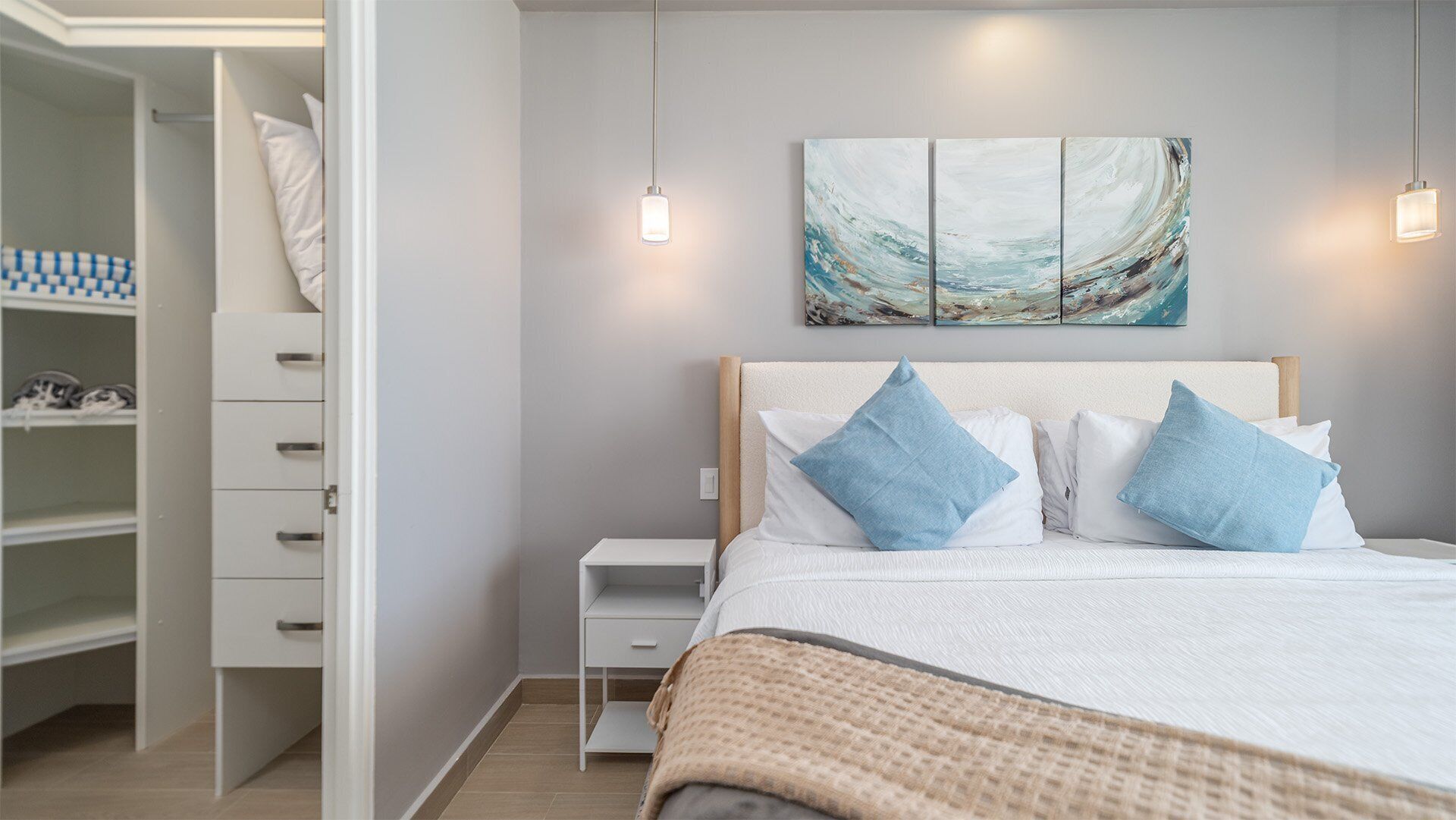 Un dormitorio ordenado con cama, mesita de noche, armario y una obra de arte en la pared.