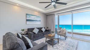 Ein modernes Wohnzimmer mit grauem Sofa, Sesseln, einem Couchtisch und Meerblick durch große Fenster.
