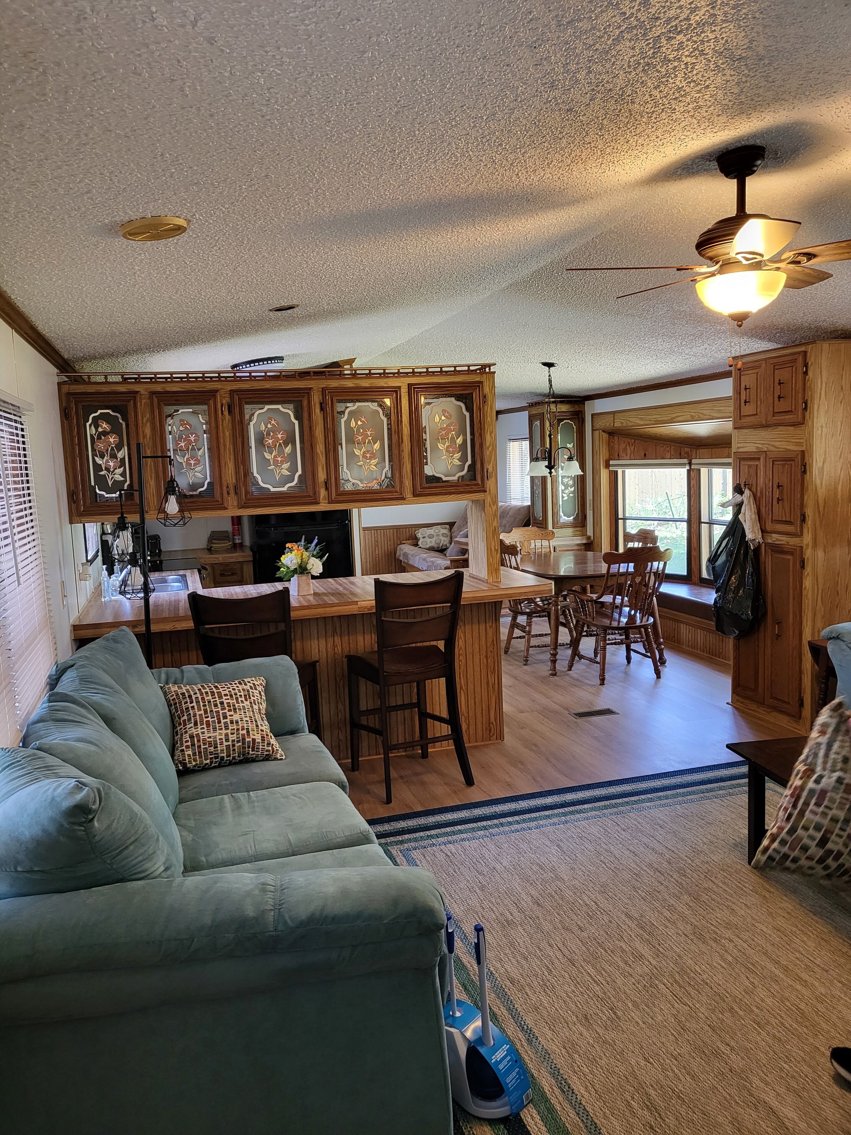 A spacious living area with a green sofa, a dining table with chairs, and a kitchen area with wooden cabinets and a bar.