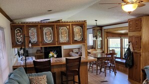 A spacious living area with a green sofa, a dining table with chairs, and a kitchen area with wooden cabinets and a bar.