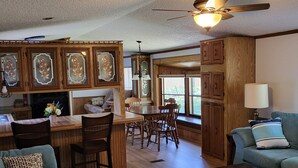 A spacious living room with a large green sofa, a coffee table, and a dining area with wooden chairs and a table.