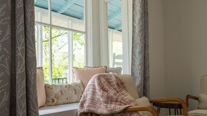 A cozy room with a window seat, wooden chair, and a view of greenery outside. - Corner Cottage, Downtown Saugatuck  (Saugatuck)