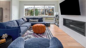 Een moderne woonkamer met een hoekbank, een voetenbankje en een open haard.