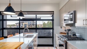Een moderne keuken met een groot eiland, roestvrijstalen apparatuur en uitzicht op gebouwen door grote ramen.