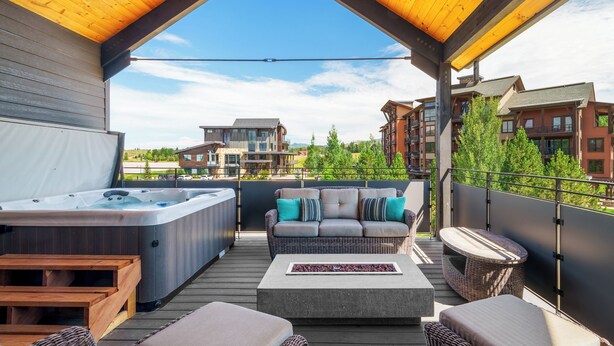Een overdekt terras buiten met een jacuzzi, rieten meubels en uitzicht op omliggende gebouwen.