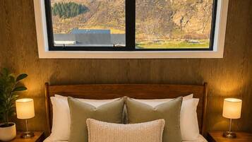A hotel room with a large bed, two nightstands, a window with a mountain view, and a potted plant.