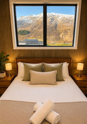 Une chambre d’hôtel avec un grand lit, deux tables de chevet, une fenêtre donnant sur la montagne et une plante en pot.