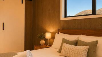 A hotel room with a large bed, a nightstand with a lamp, and a window with a view of the mountains.