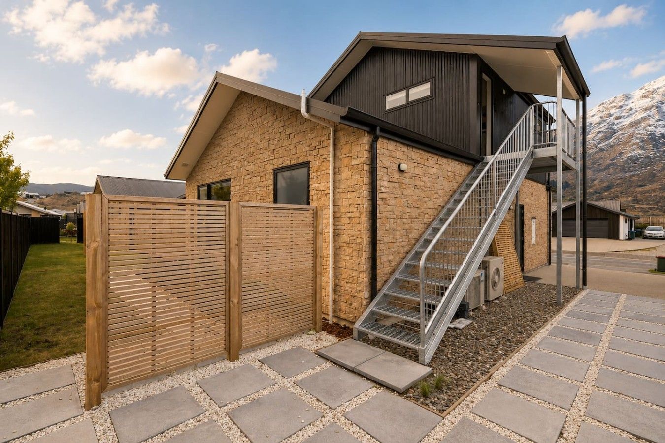 A modern building with a stone facade, a metal staircase, and a wooden fence.