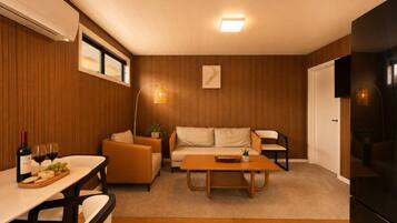 A modern living room with a sofa, armchairs, a coffee table, and a dining area with a table and chairs.