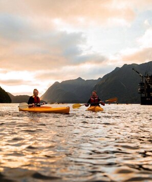 Deux personnes pratiquent le kayak sur une étendue d’eau, avec des montagnes en arrière-plan.