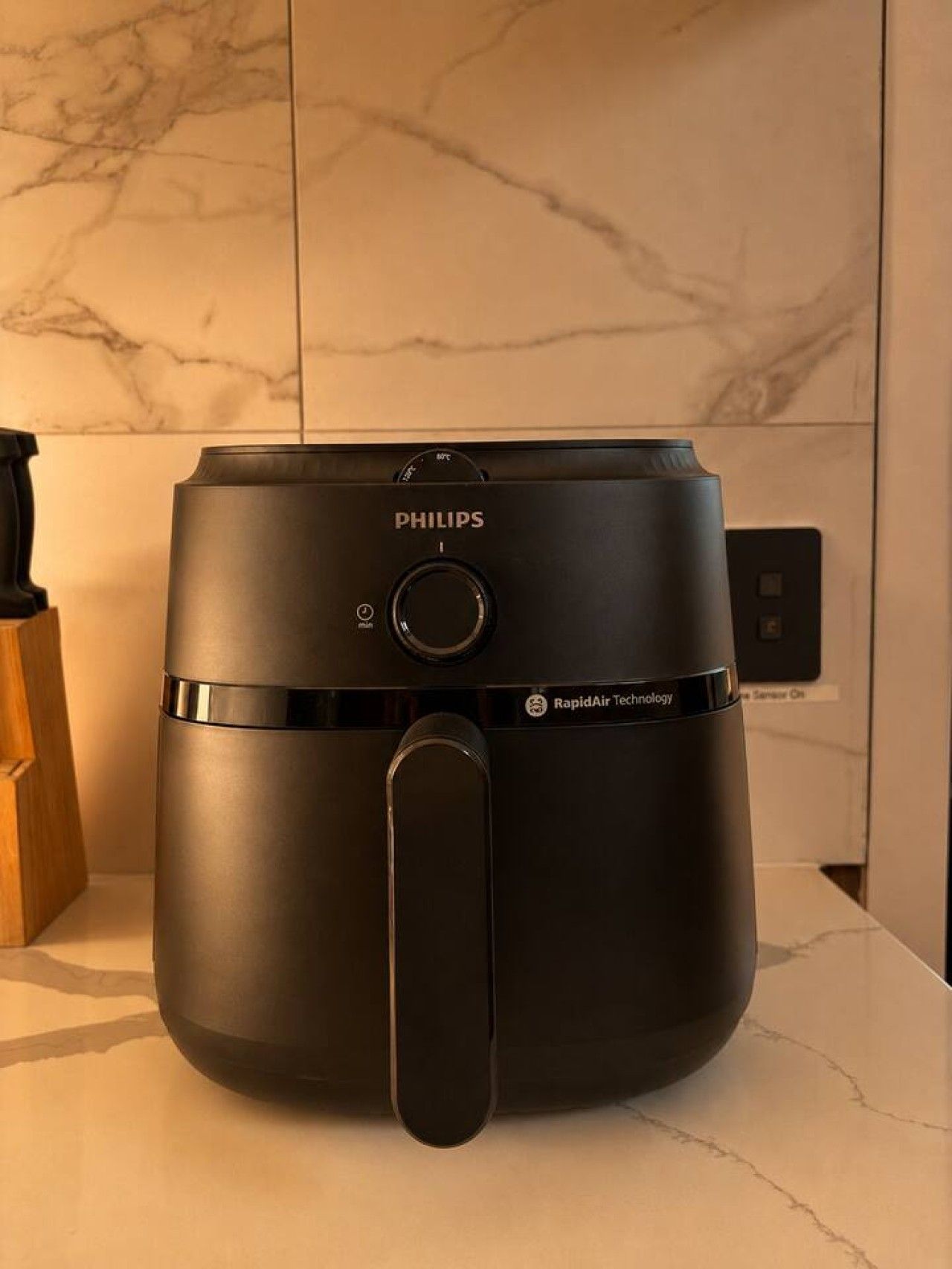 Una friggitrice ad aria Philips su un bancone da cucina con pannello di fondo in marmo.