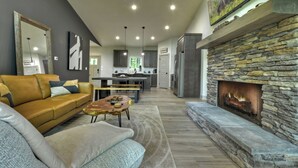 Una sala de estar moderna con chimenea de piedra, un sofá de cuero y un comedor al fondo.