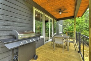 Een overdekt terras met een barbecue, een tafel en stoelen.