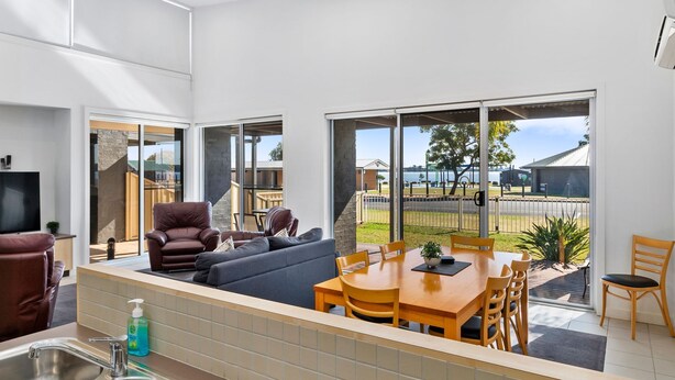 A modern kitchen with a dining area, large windows, and a view of the outdoors.