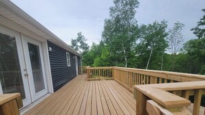 A wooden deck with a railing, a house with a sliding glass door, and trees in the background.