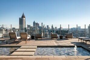 Un área de piscina en la azotea con sillones de descanso y una fuente, con vistas a un horizonte urbano.