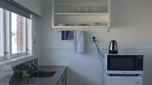 Una cucina compatta con fornelli, lavello e forno a microonde sopra un piccolo frigorifero.
