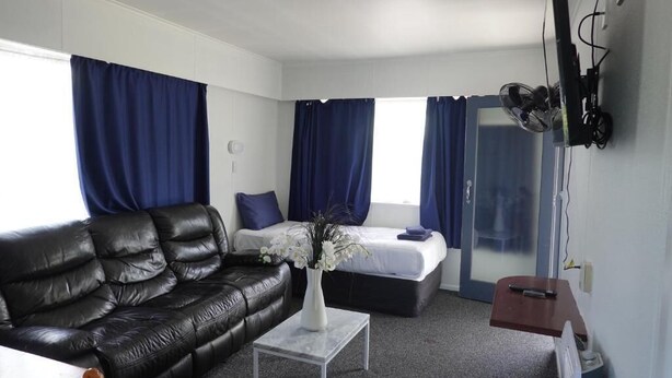 Una camera d'albergo moderna con un divano in pelle nera, un letto con tende blu, un tavolino con un vaso di fiori e una TV a schermo piatto montata a parete.