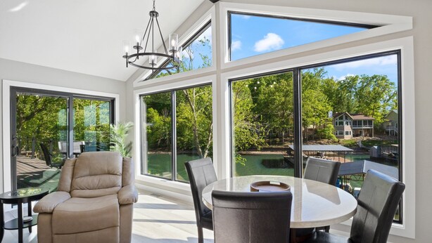 A spacious room with large windows, a comfortable chair, a dining table, and a view of a backyard with a pool. - Firepit, Hot Tub, Kayak, Games In & Out, Spacious (Gravois Mills)