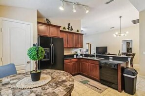 Una cocina moderna con armarios de madera, un refrigerador negro y un comedor con una mesa redonda y una planta en maceta.