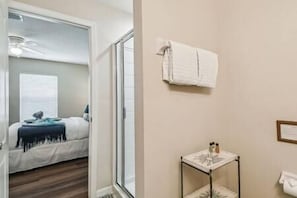 Habitación de hotel con cama, una mesita con artículos de aseo, una toalla colgada en la pared y una ventana con persianas.