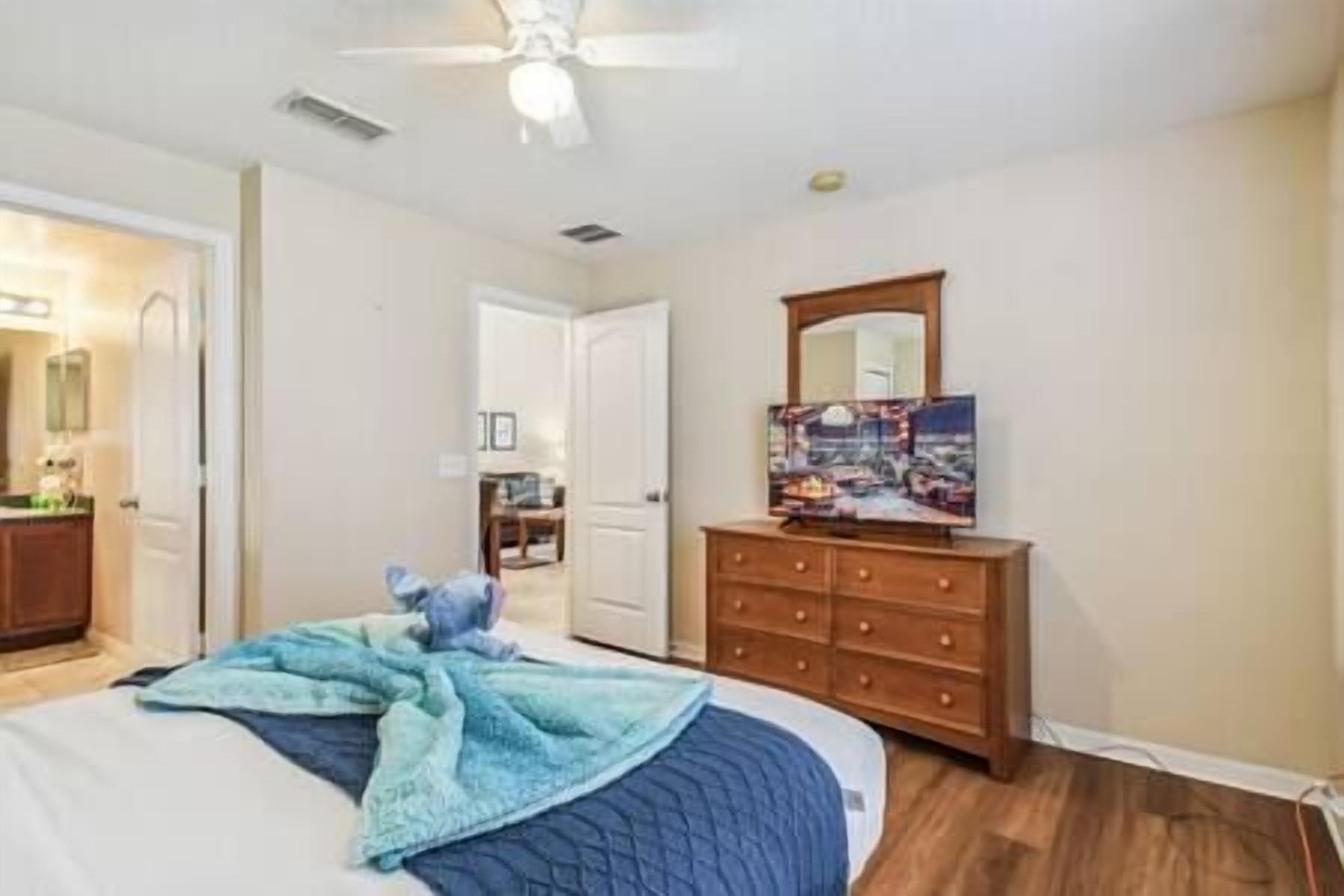 A bedroom with a bed, a dresser, a ceiling fan, and a painting on the wall.