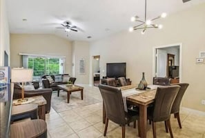 Un salón espacioso con comedor, ventilador de techo y televisor.