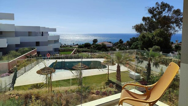 Un balcon avec vue sur la mer, une piscine et un bâtiment moderne en arrière-plan.