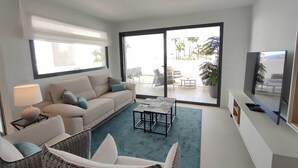 Un salon moderne comprenant un canapé, des fauteuils, une table basse, un téléviseur et une porte-fenêtre coulissante donnant sur une terrasse extérieure.