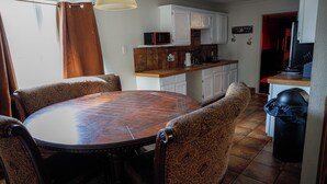 Un comedor con una mesa redonda y sillas estampadas, una cocina con armarios blancos y un microondas, además de un bote de basura.
