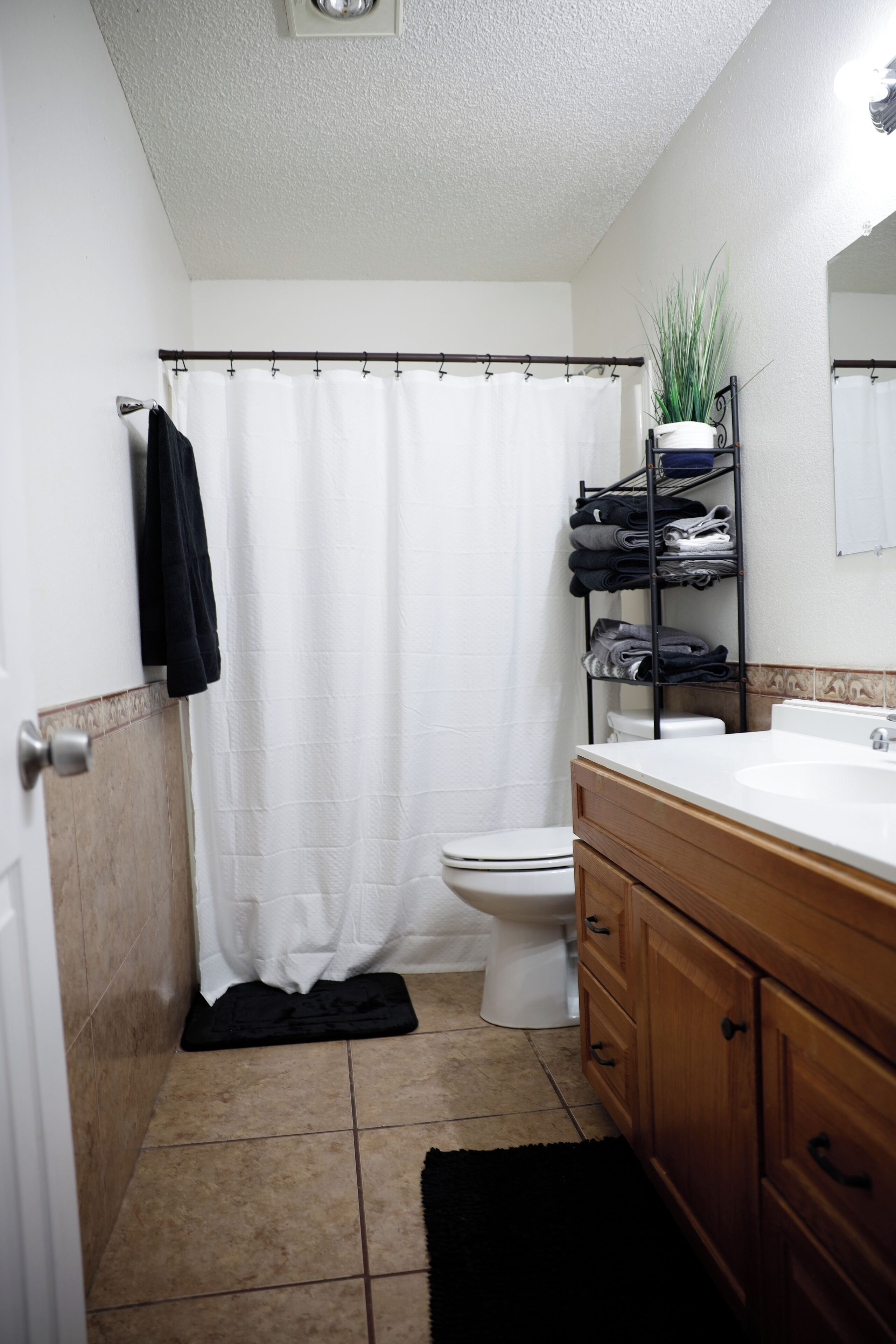 A bathroom with a white shower curtain, a toilet, a sink with a wooden vanity, and a plant on a shelf.