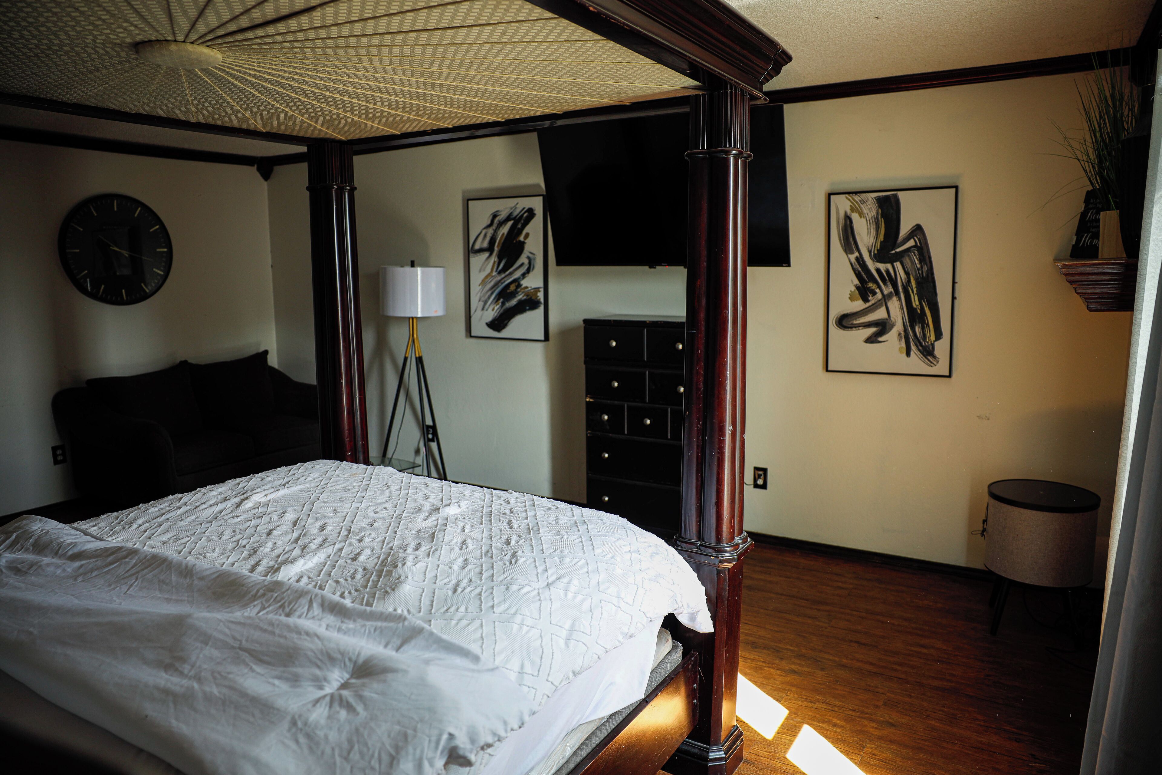Un dormitorio con una cama grande, una lámpara de pie, arte abstracto en las paredes y un reloj.