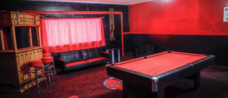 A pool table in a room with a red carpet, a wooden bar area, and a red and black color scheme.