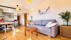 Uma sala de estar moderna com um sofá cinzento, mesa de centro de madeira e um espaço de jantar com cadeiras e uma chaleira vermelha.