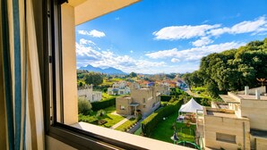 Une vue depuis une fenêtre donnant sur un quartier résidentiel, avec des bâtiments modernes, un ciel dégagé et des montagnes à l’horizon.