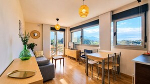 Un salon moderne avec un canapé, une table à manger et des chaises, de grandes fenêtres offrant une vue dégagée, et un vase vert posé sur une table en bois.