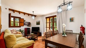 Ein Wohnzimmer mit Sofa, Fernseher, Esstisch, Stühlen und Kamin.
