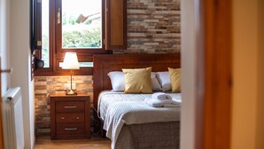 Un dormitorio con cabecera de madera, una mesita de noche con lámpara, una cama con almohadas y vistas a través de una ventana.