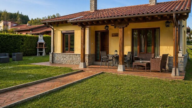 Un edificio amarillo con techo de tejas, chimeneas de piedra y un porche cubierto con mobiliario exterior.